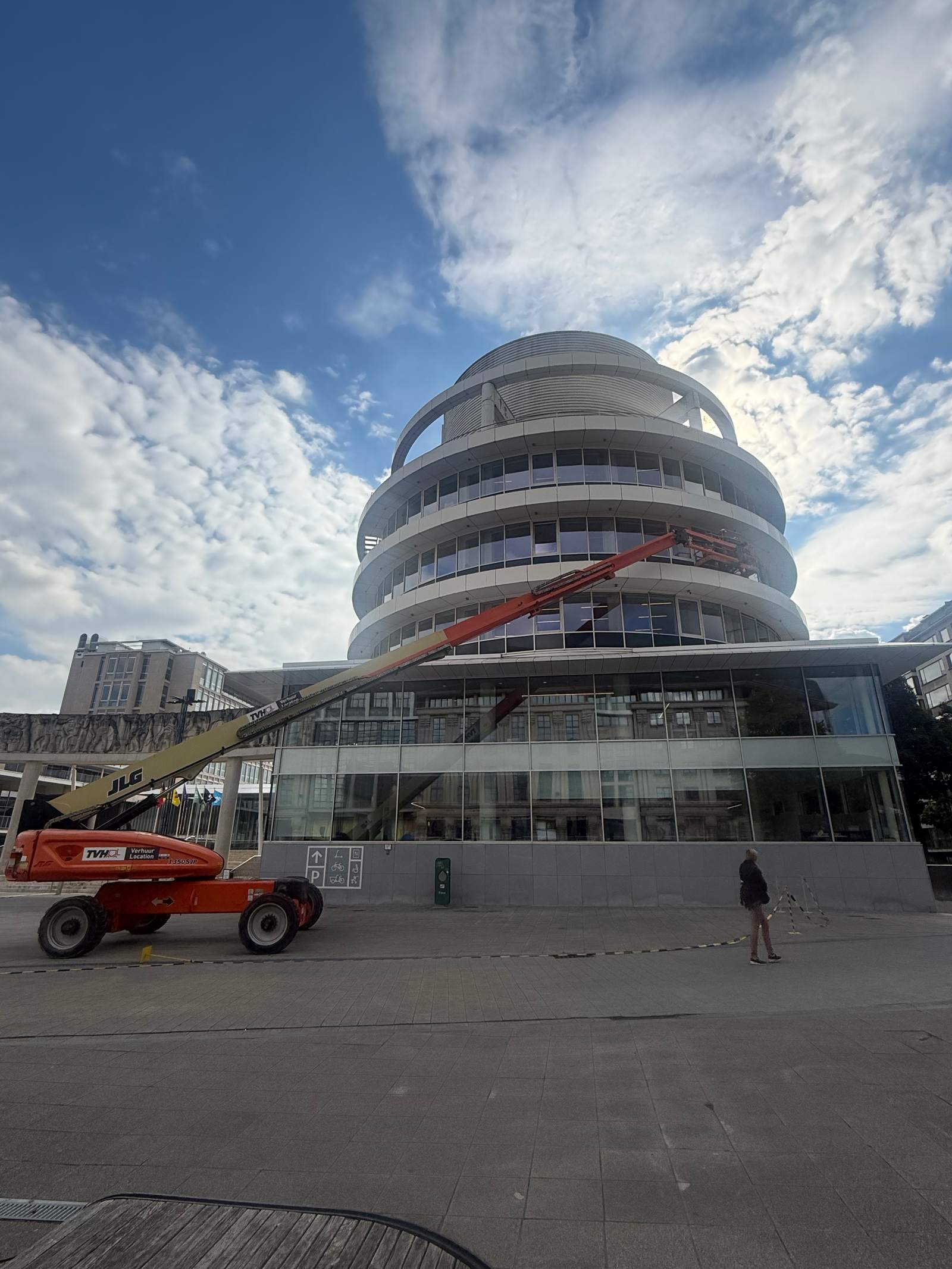 Rond gebouw met glazen gevel en een hoogtewerker ervoor